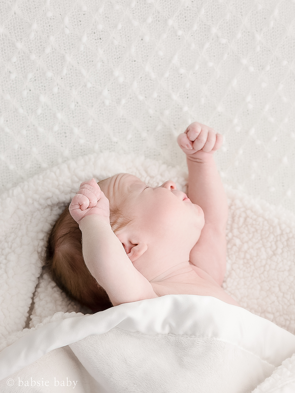 Baby girl stretching her arms at a newborn session.