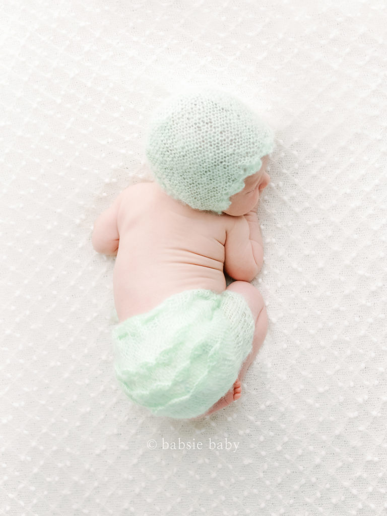 A baby girl wearing a mint baby outfit and bonnet.